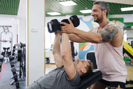 A personal trainer motivates the client to lift heavy dumbbells in the gym. Personal workout hour...