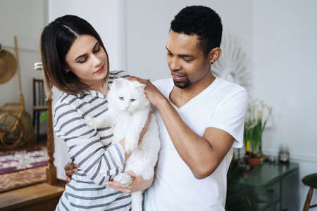 Lovely mixed-races young happy joyful couple male and female smiling in good mood resting at home in...