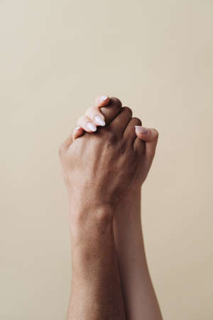Multiethnic couple holding hands. Young Caucasian woman and African male arms together on beige...