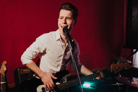 Talented handsome young guitarist man singing a song in studio recording on red background...