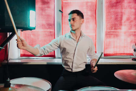 Male musician with drumsticks playing drums and cymbals at concert or studio. Music, people, musical instruments and entertainment conceptの写真素材