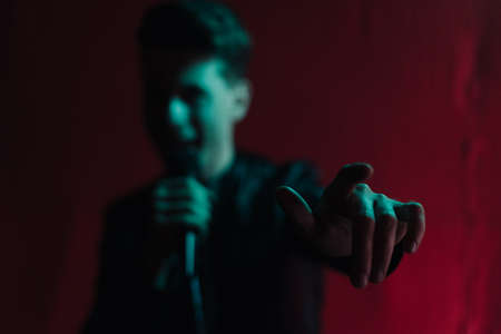 Close up portrait Rock band vocalist singing to microphone in lights on red backgroundの写真素材