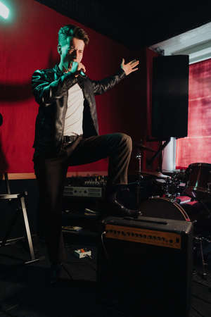 Rock band vocalist singing to microphone in lights on red backgroundの写真素材