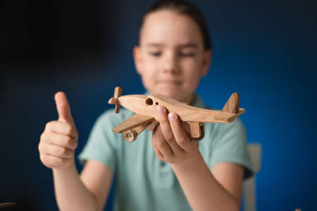 Kid boy holding an wooden plane in hands showing thumbs up. Focus on planeの写真素材