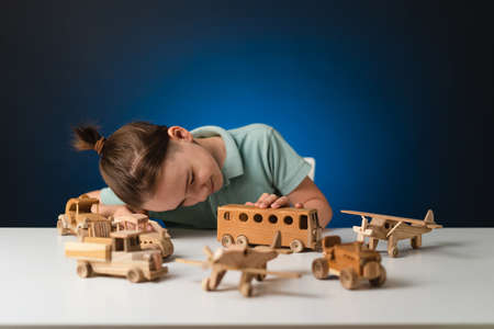 School boy playing, hands holding with wooden toys on white table, while staying at home on blue...