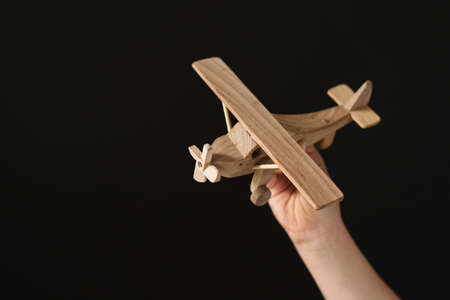 Wooden Toy airplane in hand, symbol of travel and dreams on dark background. Use for poster, card, invitation, banner, advertising, marketing, shop, print, textile, designの写真素材