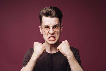 Young man holding fists up looking with determination at camera on crimson backgroundの写真素材