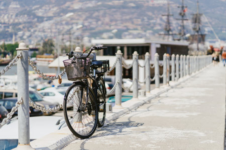Beautiful black bicycle played on seaside coast with sea, boats and city besideの写真素材