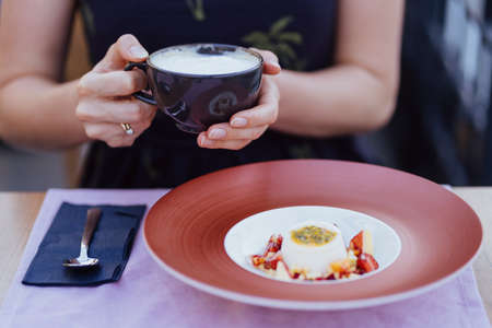 Woman holding a cup of coffee and enjoying the view of a delicious desert with fresh exotic fruitsの写真素材