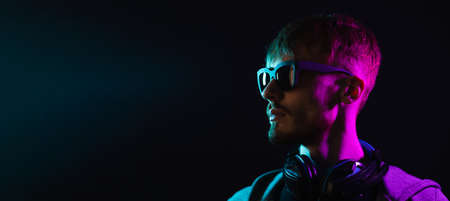 Neon portrait of a bearded man wearing headphones on the neck, wearing parka and mate sunglasses looking at copy space. Hacker portraitの写真素材