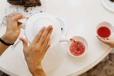 Woman hands pouring red tea from a white teapot in white cups at homeの写真素材