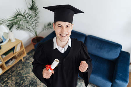 Education, graduation and people concept - happy male student with diploma at home showing his emotionsの写真素材