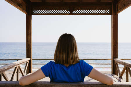 Woman in a blue t shirt enjoy the view of the sea while sitting on a wood bench