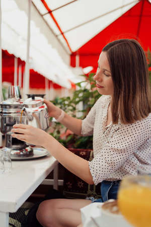 Smiling woman pouring tea from a silver pot at a Turkish breakfast on a terraceの写真素材