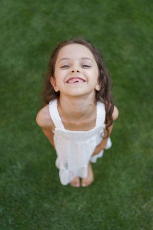Toothless portrait of beautiful little girl with smiling eyes and long brunette wavy hair looking to...