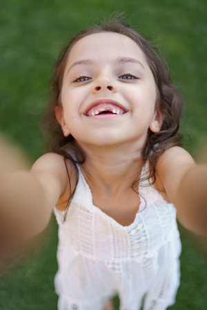 Toothless portrait of beautiful little girl with smiling eyes and long brunette wavy hair looking to...