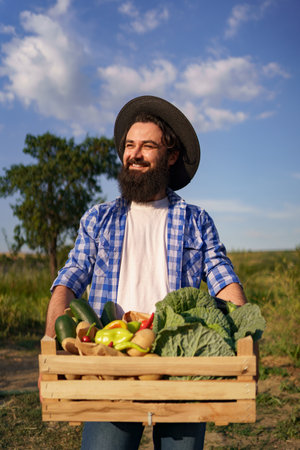 Farmer holds a wooden box with fresh veggies while walking in to his garden. Getting Ready for organic eco deliveryの写真素材