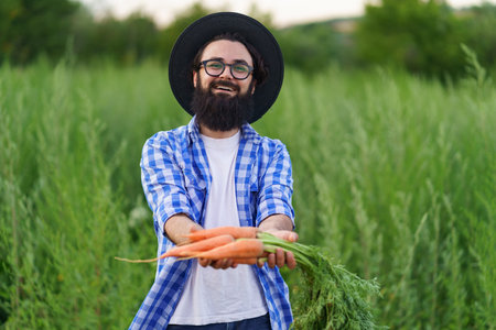 Proud farmer showing his carrots harvest to camera on green field backgroundの写真素材