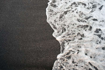 Dark sand and foamy wave background. Natural Seaside texture