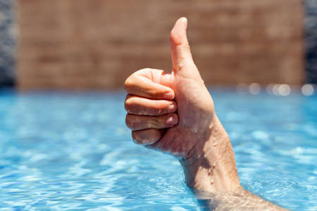 Man chilling in the water in pool and showing signs ok with his handの写真素材