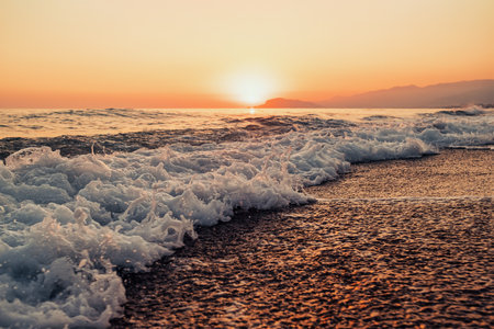 Beautiful abstract nature background with sea orange sunset on the coastline and splashing waves on...