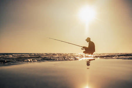 Fishermen silhouette fishing on the seashore in the evening under warm sunの写真素材