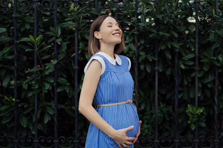 Lovely pregnant woman portrait touching happy her tummy with hands on a green leaves wall...