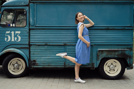 Charming pregnant womanin in a blue retro dress posing near a vintage bus with copy space.