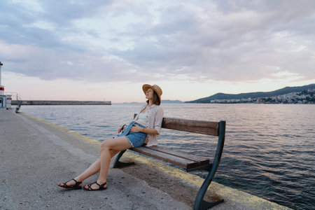 Pregnant woman on early stage resting on a bench near the sea in the morning. Healthy lifestyle, travel and relaxationの写真素材