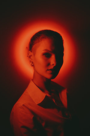 Woman portrait with glowing neon red circle on dark background looking to camera