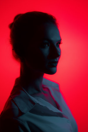 Dark woman profile portrait on red background. Lights play.の写真素材