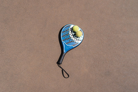 Top view of yellow padel balls placed on blue racket on brown court on sunny dayの写真素材