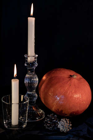 Lighted candles, in glass candlesticks. Candlelight and an orange pumpkin, on the eve of Halloween. Pumpkin, candles, dried wormwood, garlic. Protection from vampires, ghouls.の写真素材