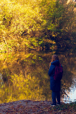 A man on the bank of a fast, small river looks into the distance. Fast water, autumn colors, golden and yellow colors in the light of the sun. Autumn, September, October, November.の写真素材