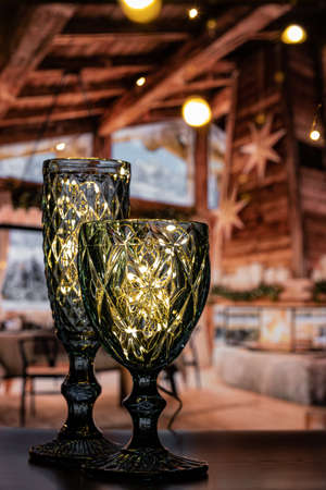 Two curly, beautiful glasses of different heights shine with light and attract attention to create a festive atmosphere. Beautiful, transparent glasses shine, Merry Christmas and Happy New Year.の写真素材