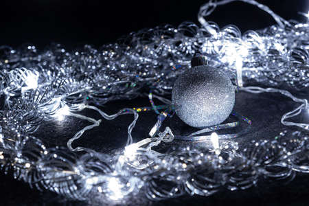 Christmas decorations: sparkling silver ball, tinsel, and garland, on a black background. Christmas...