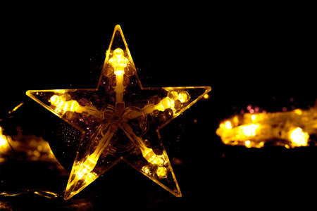 A golden five-pointed star, shining against the background of bokeh and blurred lights of garlands. A golden star, shining on a black background.の写真素材