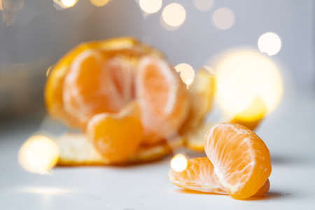 Slices of tangerine, stacked on top of each other, partially peeled tangerine and lights of garlands - in the side, on a light background. The festive mood, in anticipation of Christmas and New year,の写真素材