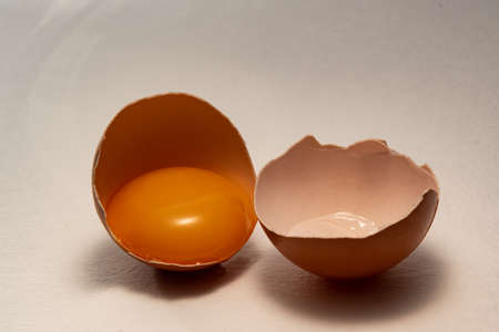 A chicken egg split in half, with the yolk in one half. The yolk, in half the shell of a chicken egg, is brown.の写真素材