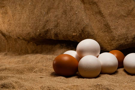 A few white and brown chicken eggs stacked in a pile. Fresh, farm, chicken eggs are stacked in a pile, on a textured substrate - burlap.の写真素材