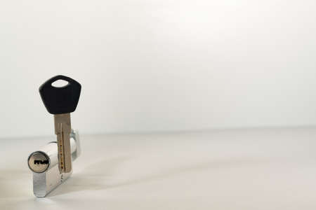 The key to the lock, next to the keyhole. A flat key, next to the larva from the lock, on a white...