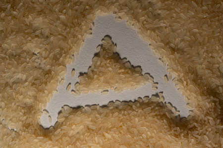 Textured rice grains, poured in one layer, form a textured surface on which the letter "A" is printed. Grains of white, long-grain, steamed rice.の写真素材