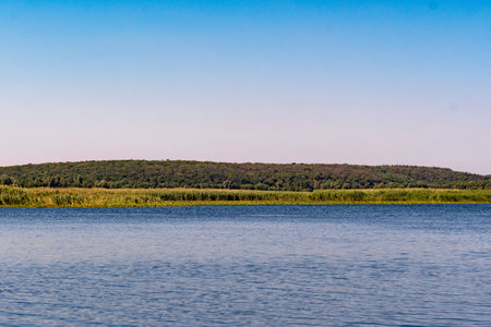 A large pond with clear water and green vegetation on the horizon. A picture of the water surface, the shore and the sky. The picture consists of three parts, a pond in the lower pの写真素材