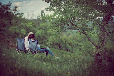 A couple in love is sitting on a hill, in folding chairs and talking. A guy and a girl are sitting with their backs to the camera and talking about love.の写真素材