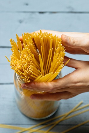 Womans hands holding spaghetti in a glass jar on a wooden vintage light backgroundの写真素材