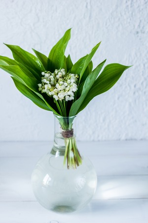 Bouquet of lily of the valley in a little transparent vase on wooden light background. Fresh spring moodの写真素材