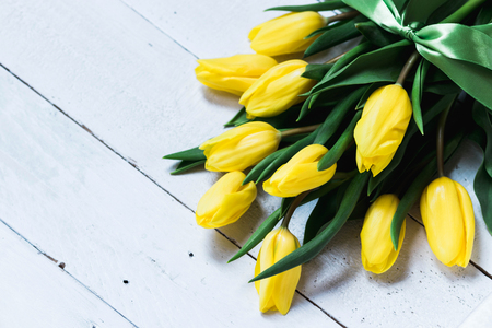 Spring decorative composition. Bouquet of yellow tulips tied by green ribbon. Close up portrait on white wooden background.の写真素材