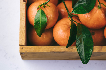 Tangerines oranges, clementines, citrus fruits with green leaves in a wooden box over light background with copy spaceの写真素材