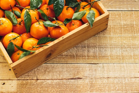 Tangerines oranges, clementines, citrus fruits with green leaves in a wooden box over light wooden background with copy spaceの写真素材