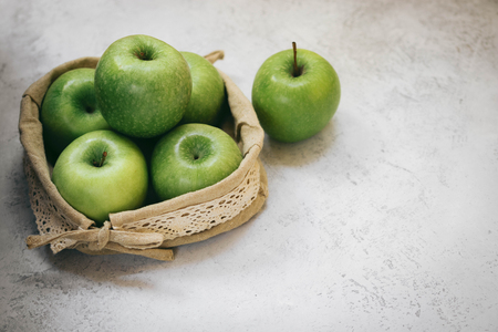 Green apples in a woven small bag on a light background.の写真素材